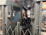 A guy wearing a suit standing on the outside part of the vestibule between the two Arnine Cars